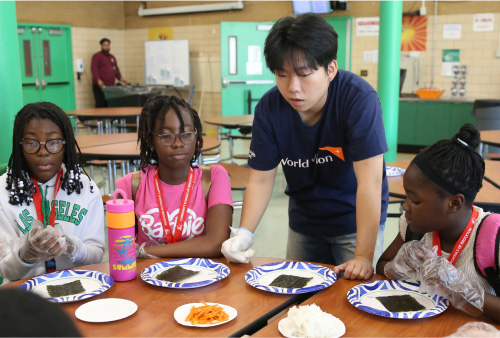 김밥을 만들기 위해 재료를 펼쳐놓고 설명을 듣는 아이들과 가르쳐 주는 봉사자